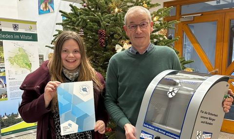Wirtschaftsförderin Angela Seidel und Bgm. Erwin Geitner bei der AED-Bescheidübergabe an die Gemeinde Rieden vor einem Weihnachtsbaum